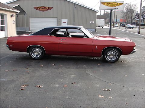1969 Ford Torino - A red 1969 Ford Torino coupe with a black vinyl top is parked in front of a building.