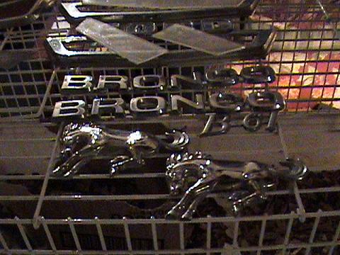 1986 Ford Bronco - Chrome Ford Bronco emblems and horse emblems are displayed on a wire rack.