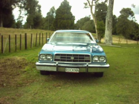 1973 Ford Ranchero - A blue sedan is parked on a grassy field with trees in the background.