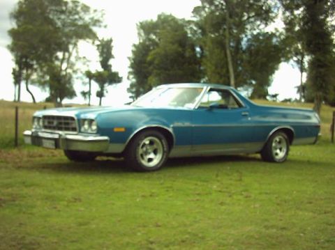 1973 Ford Ranchero - A blue 1973 Ford Ranchero sits on a grassy field with trees in the background.