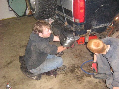 1995 Ford Bronco - Mechanics are performing maintenance on the rear axle of an SUV in a garage setting.
