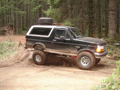 1996 Ford Bronco - A lifted 1996 Ford Bronco navigates a muddy trail through a dense forest.