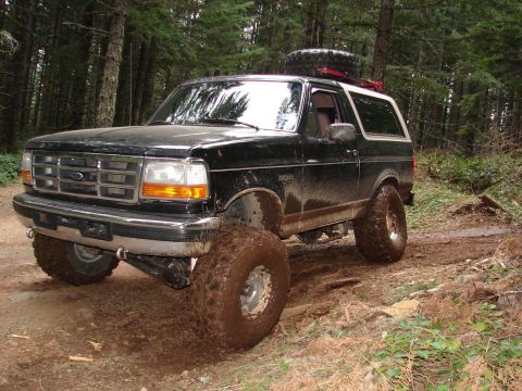 1996 Ford Bronco - This 1996 Ford Bronco navigates a challenging muddy trail through a wooded area, equipped with large off-road tires and a spare tire on the…