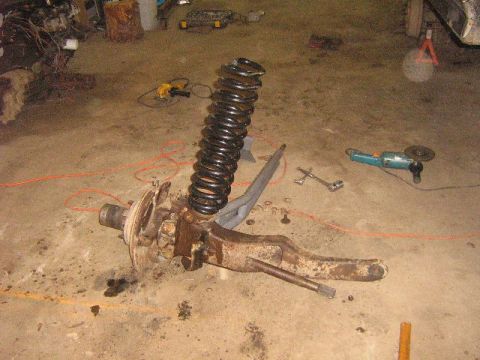 1995 Ford Bronco - A vehicle's suspension component, likely from the front axle, is disassembled and lying on the ground with tools nearby.