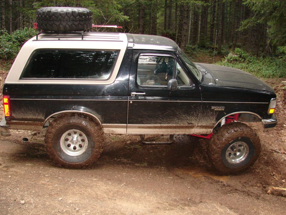 Black and tan Ford Bronco with lifted suspension and off-road tires on a dirt trail