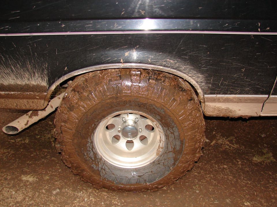 Mud-covered tire and fender of a dark-colored vehicle, with exhaust pipe visible