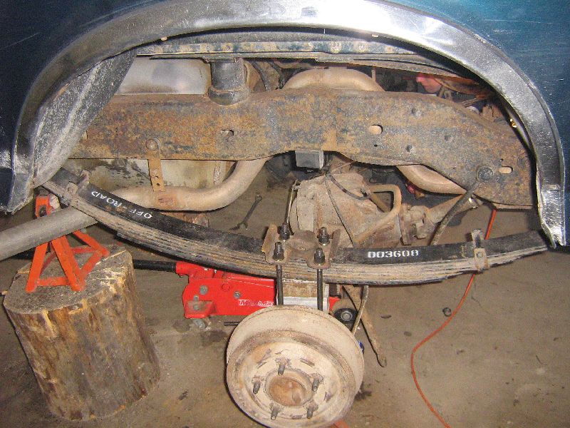 Rear leaf spring suspension with "OFF-ROAD" and "003608" markings, supported by a log and jack