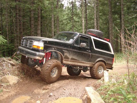 1996 Ford Bronco - This lifted 1996 Ford Bronco navigates a challenging muddy trail through a forest.