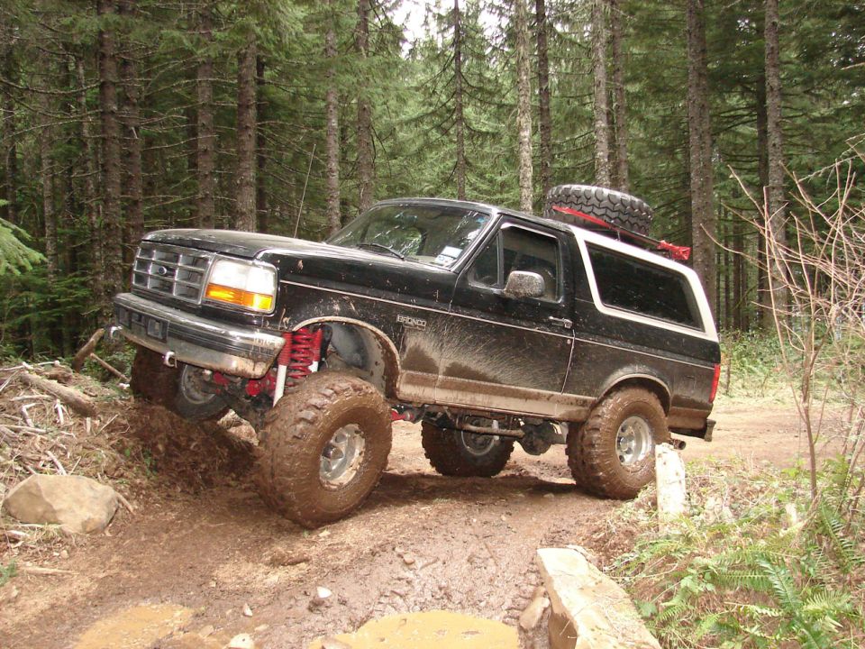 1996 Ford Bronco on a muddy trail with lifted suspension and off-road tires
