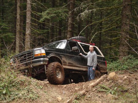1996 Ford Bronco - A person stands next to a lifted black Ford Bronco navigating a wooded trail.