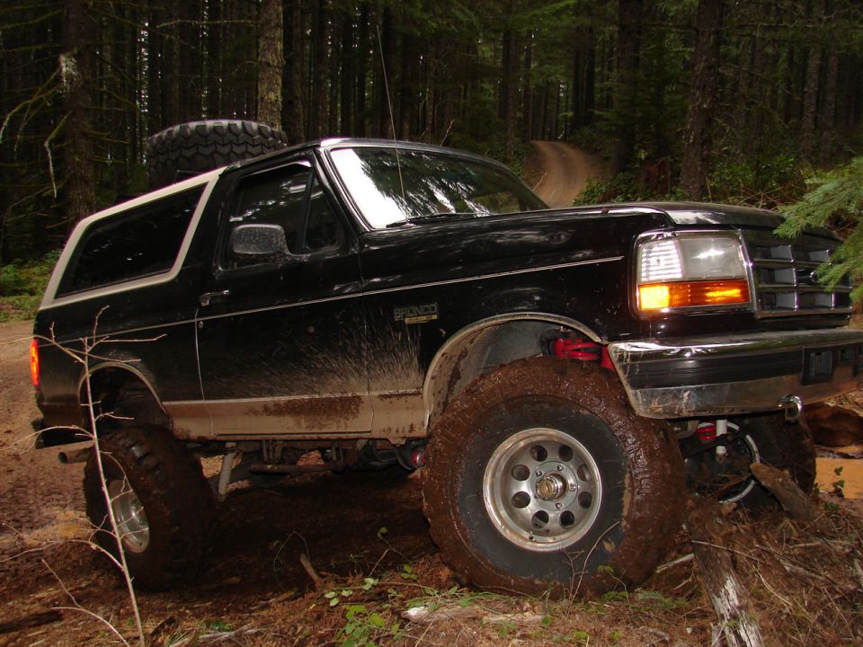 Black 1996 Ford Bronco with lifted suspension navigating a muddy forest trail