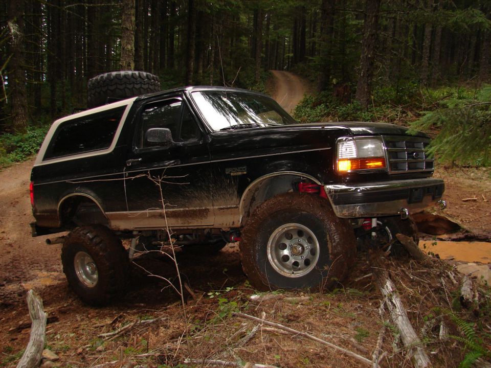 Black 1996 Ford Bronco driving on a muddy trail in a forest