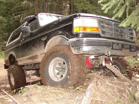 1996 Ford Bronco - A black Ford Bronco navigates a muddy, wooded trail with its tires deep in the dirt.