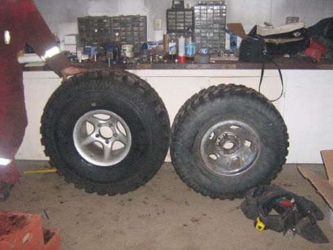 1995 Ford Bronco - Two off-road tires and wheels are displayed in a garage setting, with a workbench and tool organizers in the background.