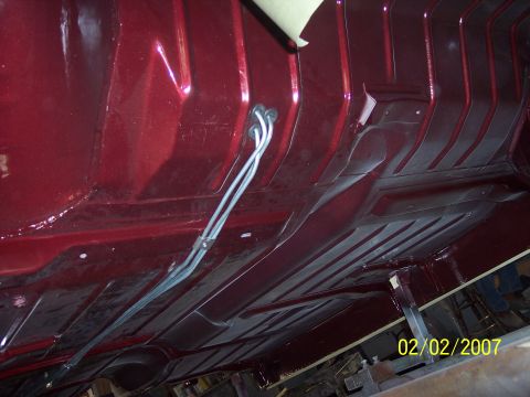 1960 Ford Falcon - The undercarriage of a red vehicle is shown, with prominent structural ribs and fuel lines visible.