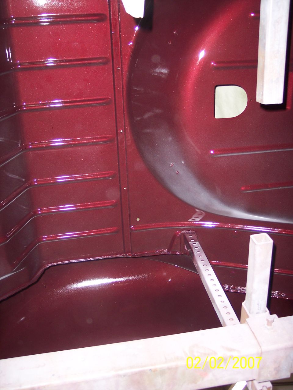 Freshly painted maroon trunk floor and rear wheel tub on a body shell in restoration