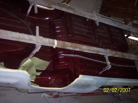 1960 Ford Falcon - The underside of a vehicle is being painted a deep red color, with protective coverings in place.