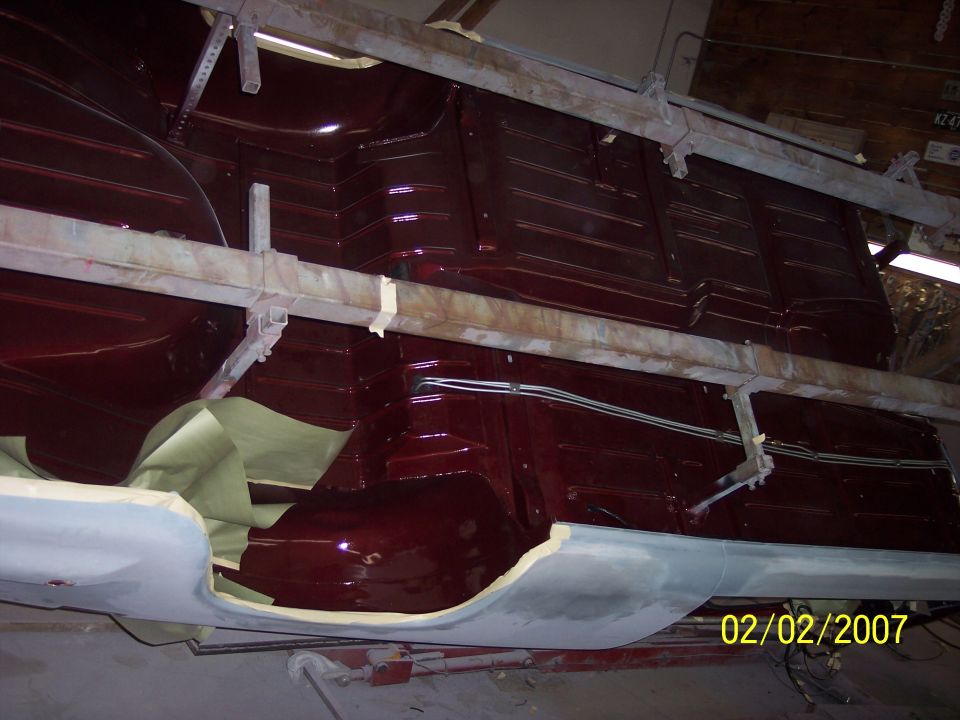 Stripped body shell with gloss maroon floor pan on a body cart during restoration