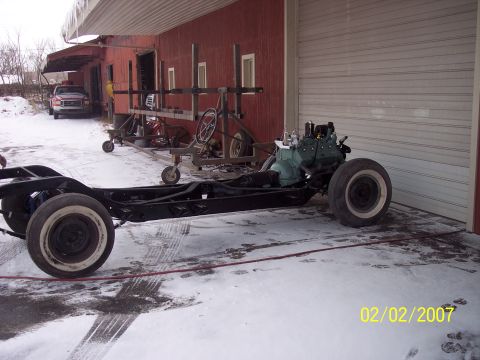 1960 Ford Falcon - A vehicle chassis with an engine is parked outside a garage in snowy conditions.