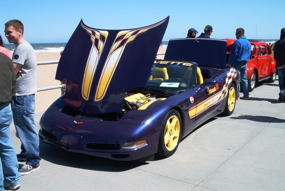 Purple Corvette C5 Pace Car convertible with yellow wheels and raised hood at a beachfront car show