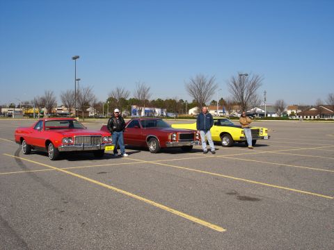 1979 Ford Ranchero - Three men stand with three cars, including a red 1979 Ford Ranchero, in a parking lot.