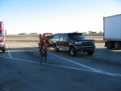 1952 Ford Pickup - A Ford Bronco SUV tows a trailer with a truck, seen at a rest stop with other large vehicles.