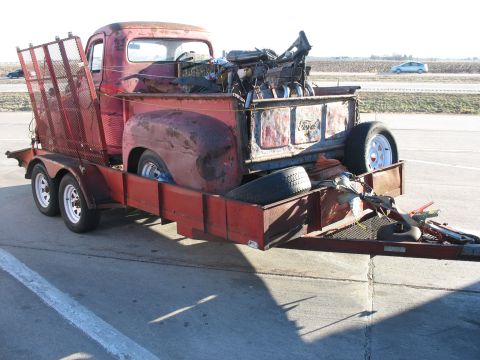 1952 Ford Pickup - A vintage red pickup truck, loaded with various parts, is being transported on a trailer down a highway.