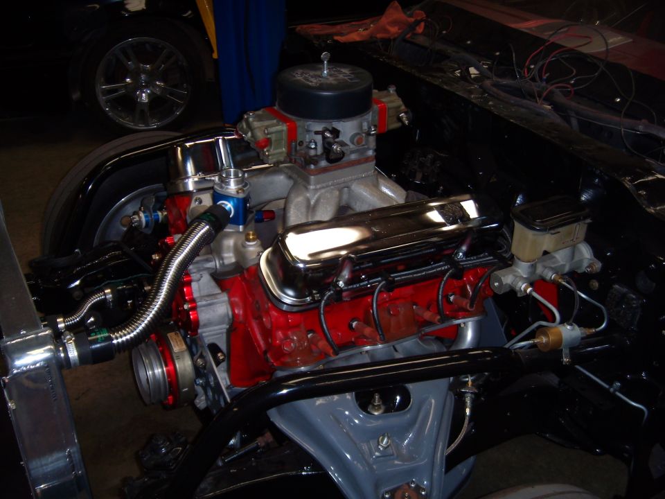 Close-up of a V8 engine with chrome valve covers, dual carburetors, and red block