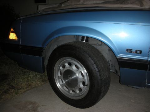 1990 Ford Mustang - Close-up of a blue 1990 Ford Mustang's side, highlighting the wheel and the "5.0" emblem on the fender.