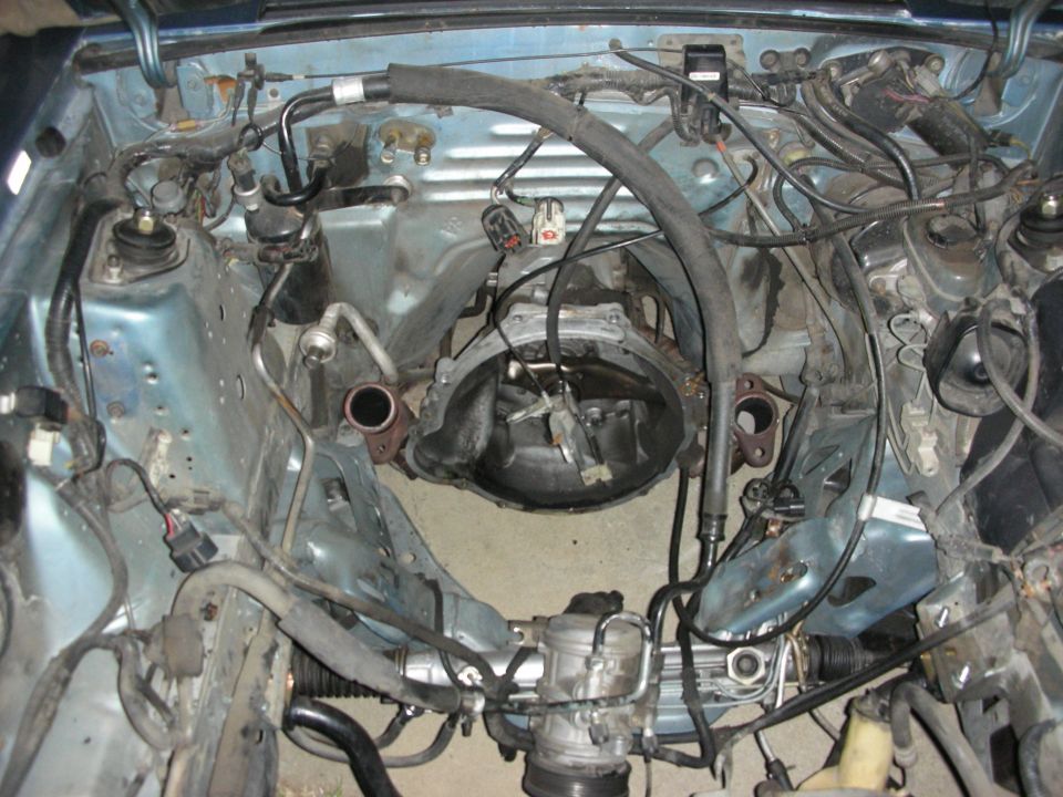 Engine bay of a car with transmission removed, showing frame rails, steering rack, and engine mounts