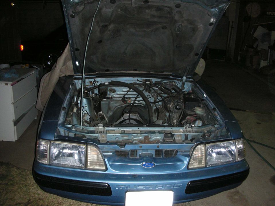 Blue Ford Mustang with hood open showing engine bay. "Mustang" text visible on front bumper