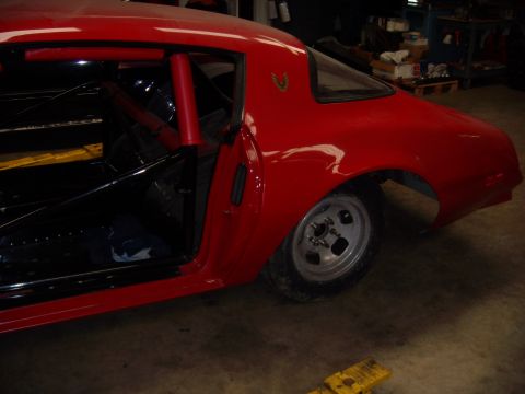 1984 Ford Bronco - A red 1977 Pontiac Firebird is shown from the rear quarter angle, modified with a roll cage and racing wheels.