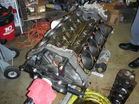 1990 Ford Mustang - A disassembled engine block sits on a stand in a workshop, surrounded by tools and other engine components.