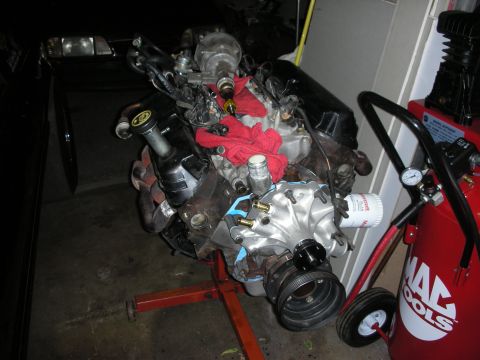 1990 Ford Mustang - Engine on a stand next to a black car and a red air compressor.