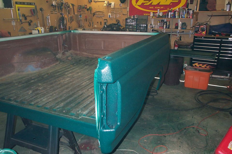 Green truck bed and rear fender on sawhorses in a garage, with tools on the wall
