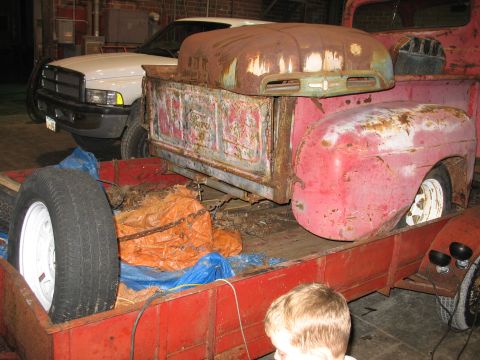 1952 Ford Pickup - A vintage pickup truck bed and hood, heavily rusted, sit on a trailer next to a modern white pickup truck.