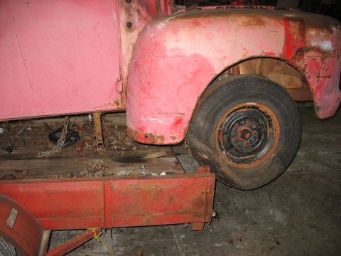 1952 Ford Pickup - A red pickup truck's front fender and flat tire are visible, resting on a trailer.