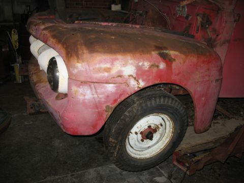 1952 Ford Pickup - The front end of a weathered red pickup truck shows significant rust and wear, with one headlight visible.