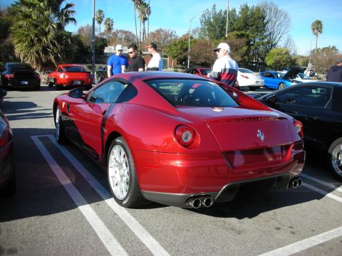 1998 Ford Crown Victoria - red Ferrari coupe seen from the rear three-quarter, dual round taillights and quad exhaust, with people standing nearby.