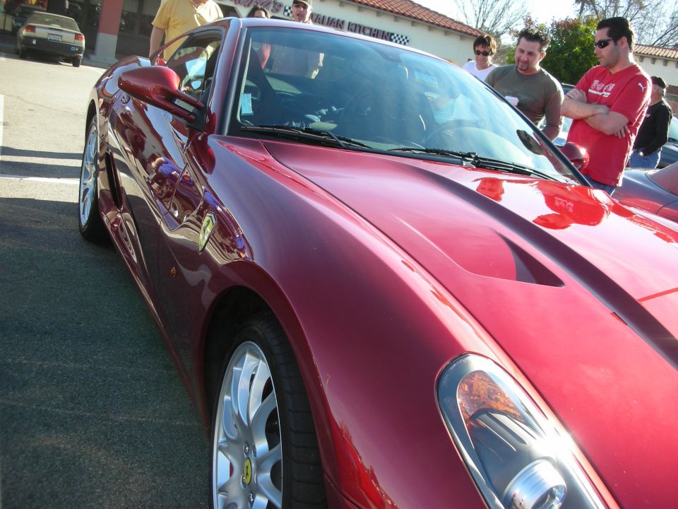 Front side view of a dark red Ferrari coupe with onlookers