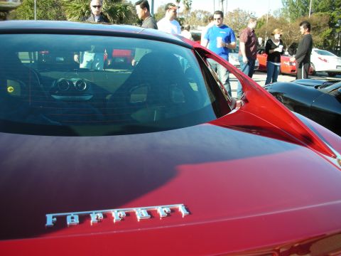 1998 Ford Crown Victoria - rear deck and window of a red Ferrari with chrome Ferrari script badge, people gathered behind in a lot.