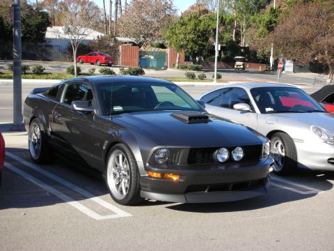 1998 Ford Crown Victoria - charcoal-gray Ford Mustang GT with hood scoop, twin round driving lights and chrome wheels parked in a lot.