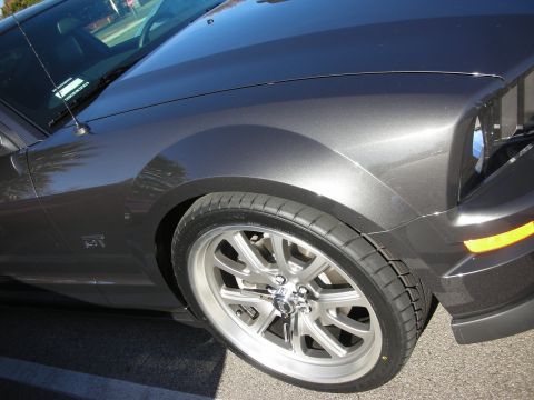 1998 Ford Crown Victoria - Close-up of a dark charcoal Ford Mustang GT's front fender, headlamp, and machined five-spoke alloy wheel in sunlight.