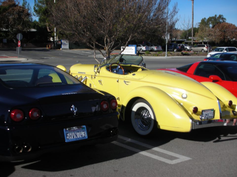 Yellow boattail roadster between black Ferrari and red car in parking lot