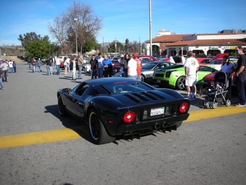 1998 Ford Crown Victoria - Rear view of a black Ford GT with its round dual taillights, parked along a yellow curb amid crowds at an outdoor car show.