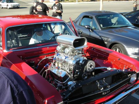 1998 Ford Crown Victoria - Engine bay of a maroon muscle car showing a polished supercharger and chrome scoop, with a man and other cars in the background.