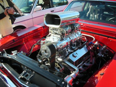 1998 Ford Crown Victoria - chrome supercharger and air scoop dominate a red muscle car's engine bay, with a red Mustang parked behind.