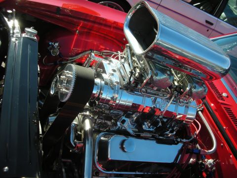 1998 Ford Crown Victoria - Close-up of a polished chrome supercharger with air scoop and serpentine belt atop a red muscle car's chromed engine.