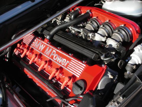 1998 Ford Crown Victoria - Detailed close-up of a red BMW M Power inline-six engine showing the valve cover and individual throttle-body intake runners.