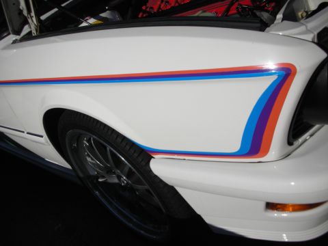 1998 Ford Crown Victoria - white Ford Mustang's rear quarter panel decorated with a multicolor red-orange-blue-purple side swoosh stripe over the wheel.